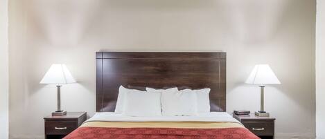 A hotel room with a large bed, two bedside tables with lamps, a wooden headboard, and a red patterned bedspread.