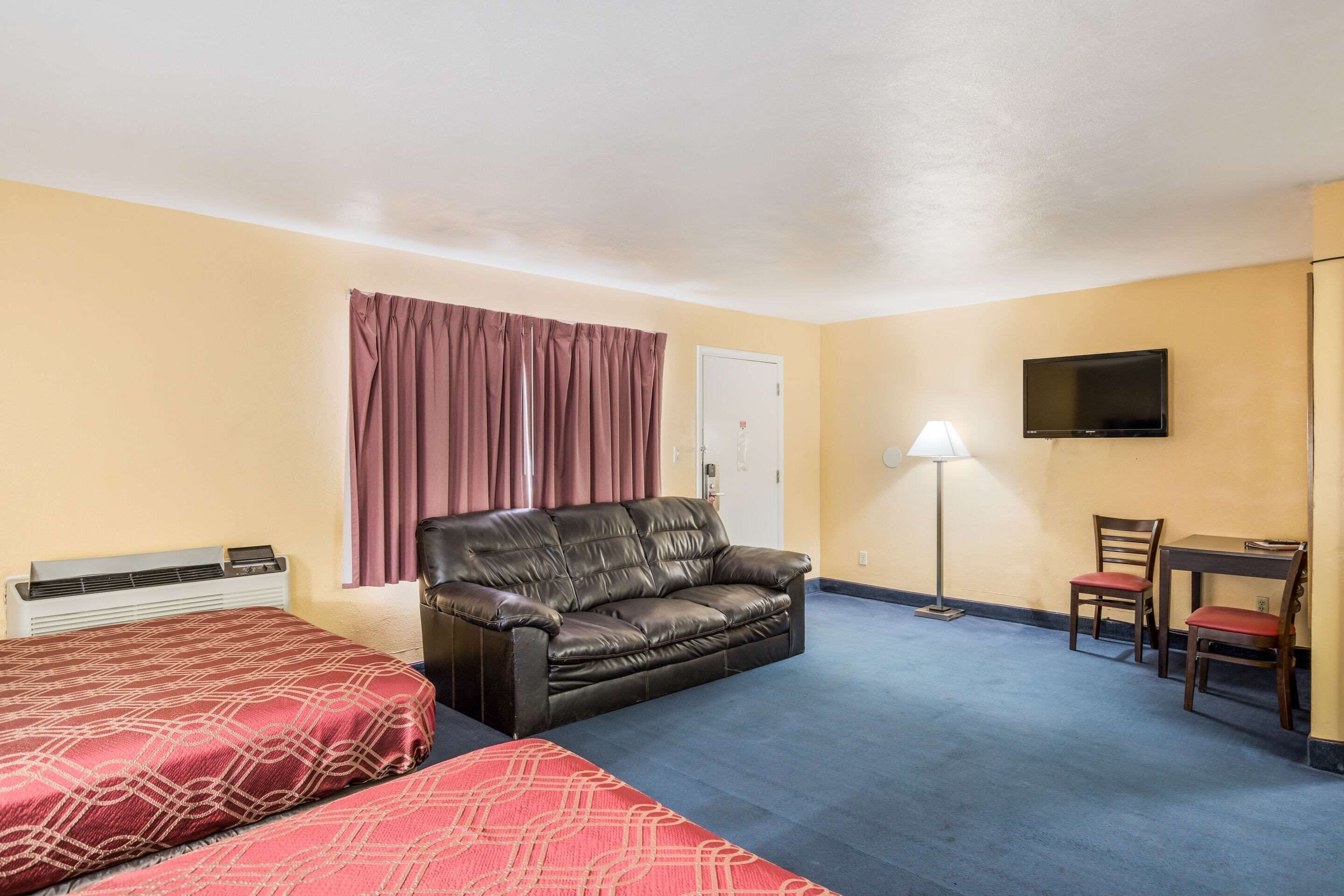 Habitación de hotel con cama, sofá, escritorio con silla, televisor y lámpara.
