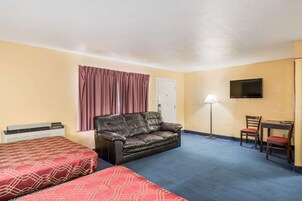 Habitación de hotel con cama, sofá, escritorio con silla, televisor y lámpara.
