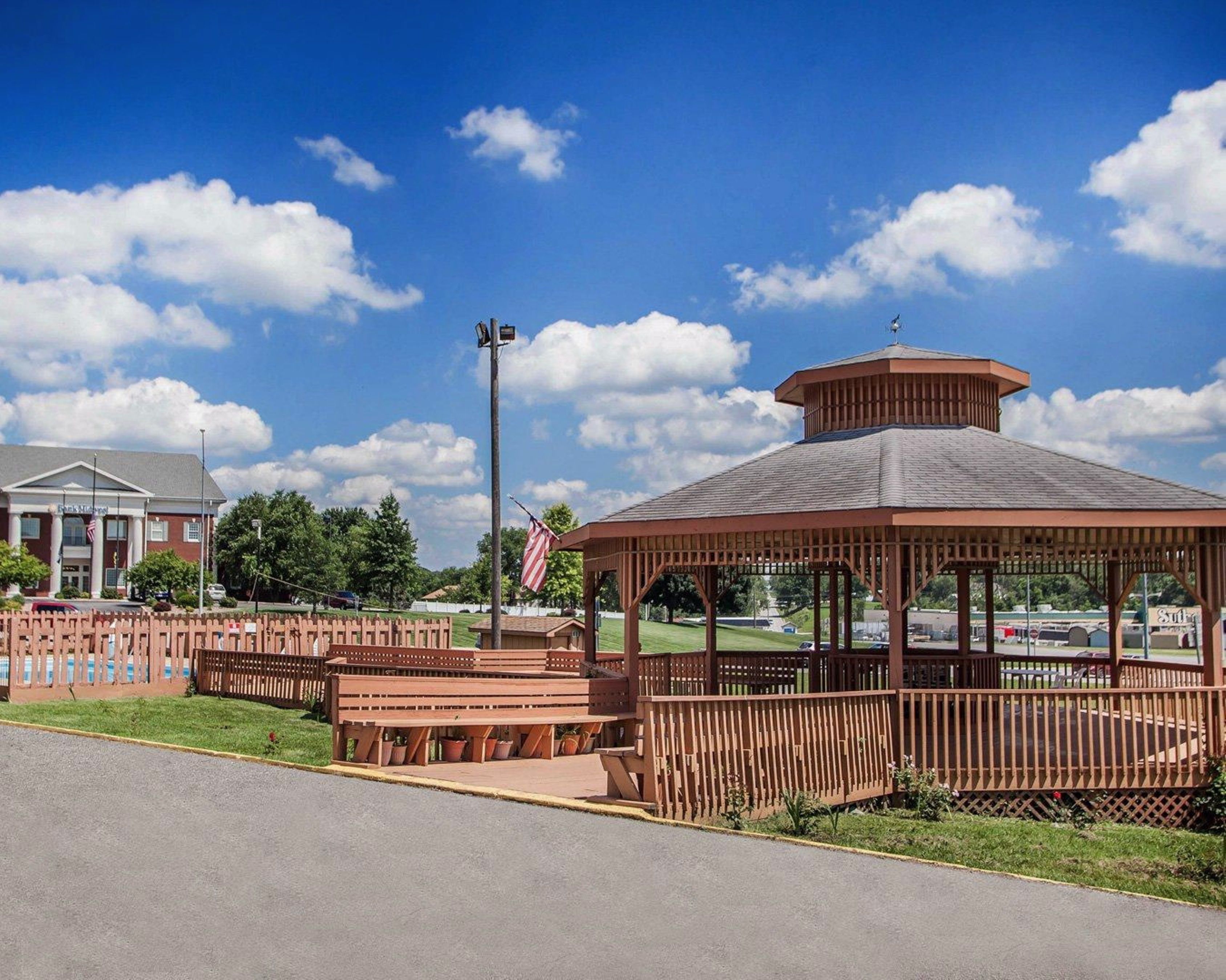A gazebo with a wooden structure and a roof, surrounded by a fence and potted plants.