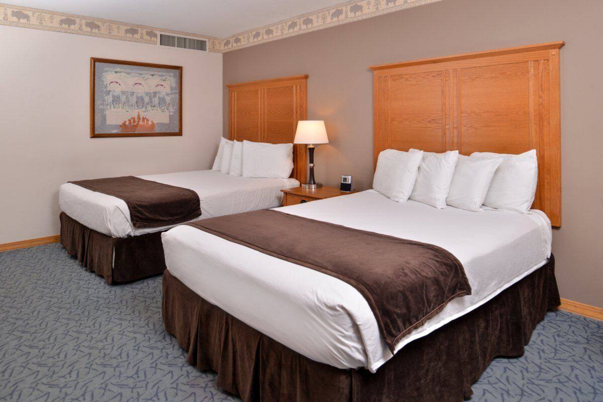 Quarto de hotel com duas camas, uma mesa de cabeceira, um abajur e um quadro na parede.