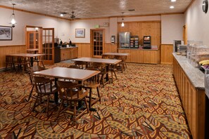 A dining area with wooden tables and chairs, a patterned carpet, and a kitchen area with appliances.