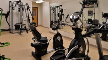 A gym with various exercise machines, including treadmills and weight equipment, and a large mirror reflecting the space.