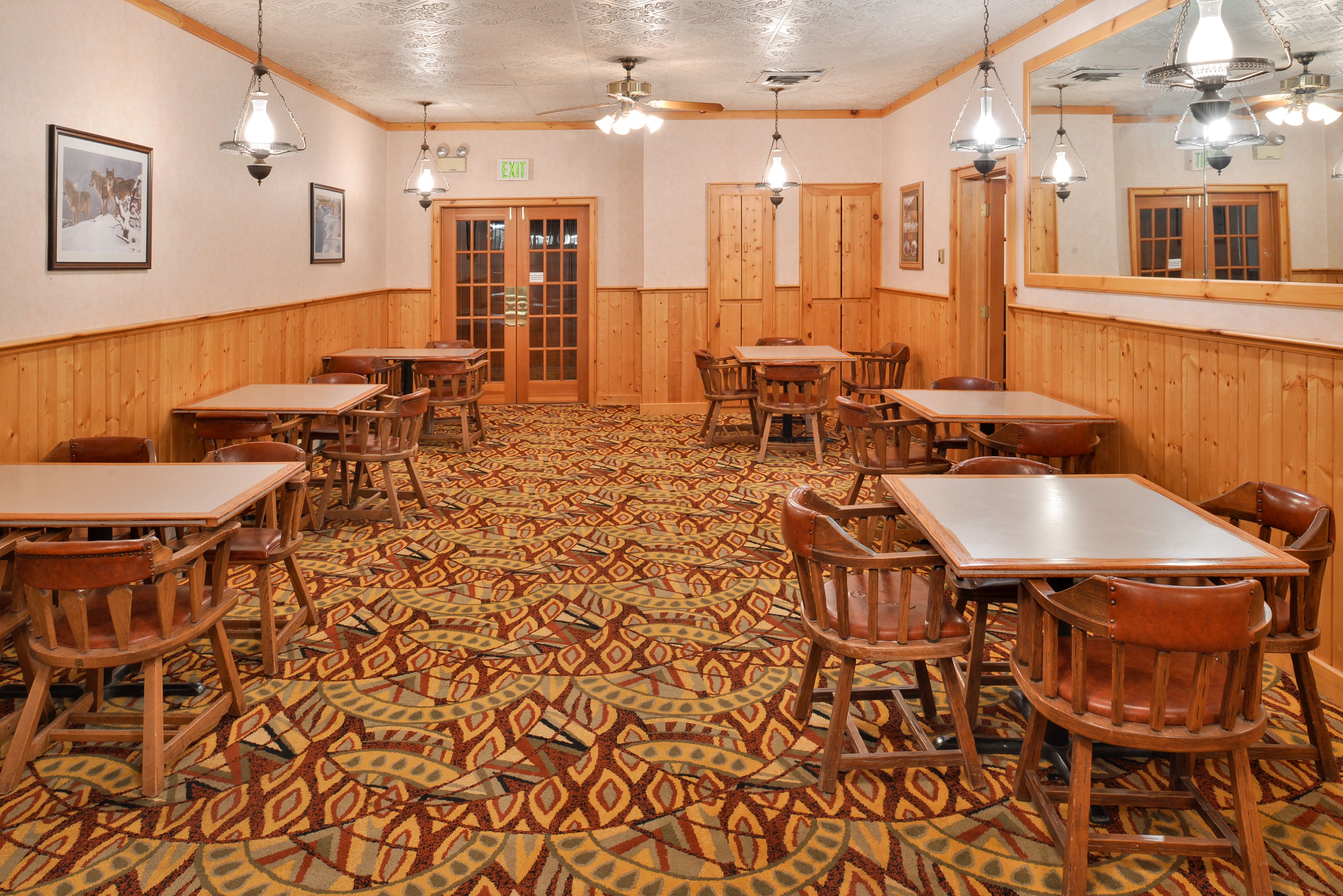 A restaurant with wooden paneling, patterned carpet, and multiple tables and chairs.