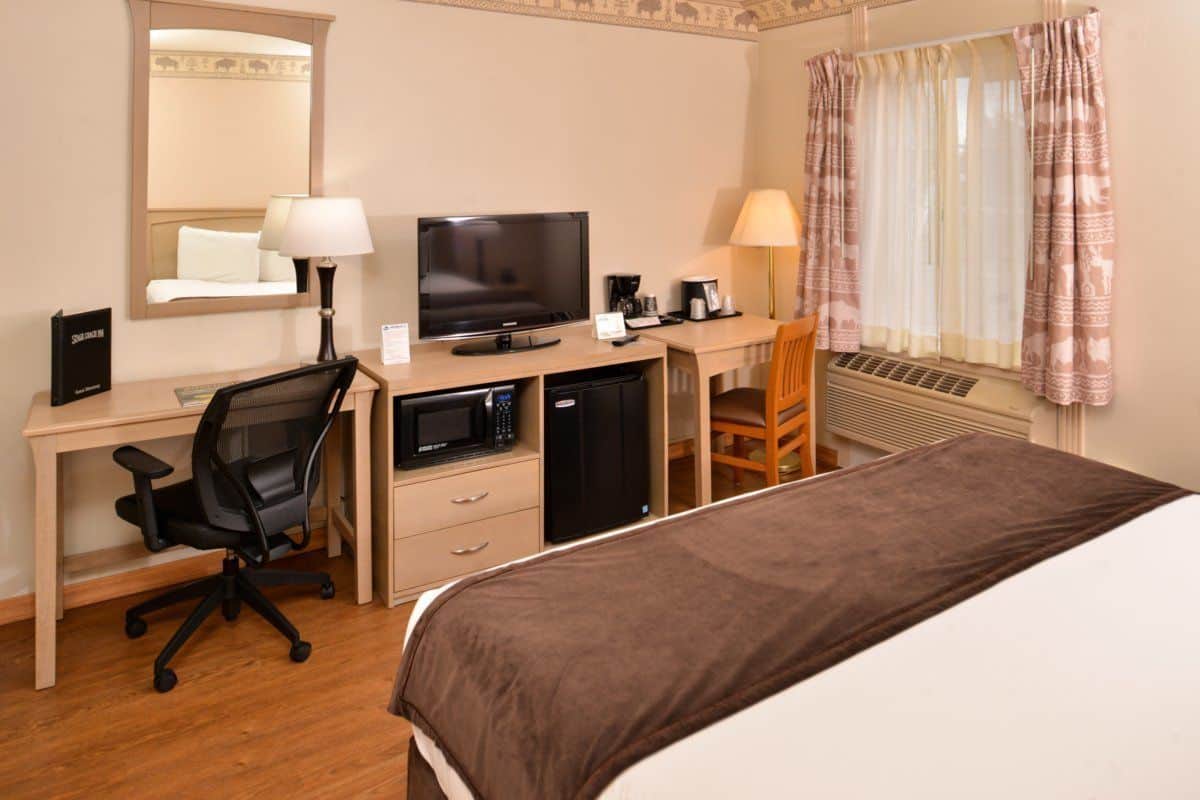 Quarto de hotel com cama, escrivaninha, cadeira, televisão, micro-ondas e ar condicionado.