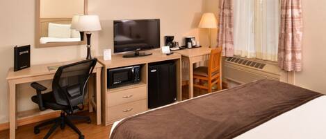 A hotel room with a bed, desk, chair, television, microwave, and air conditioning unit.