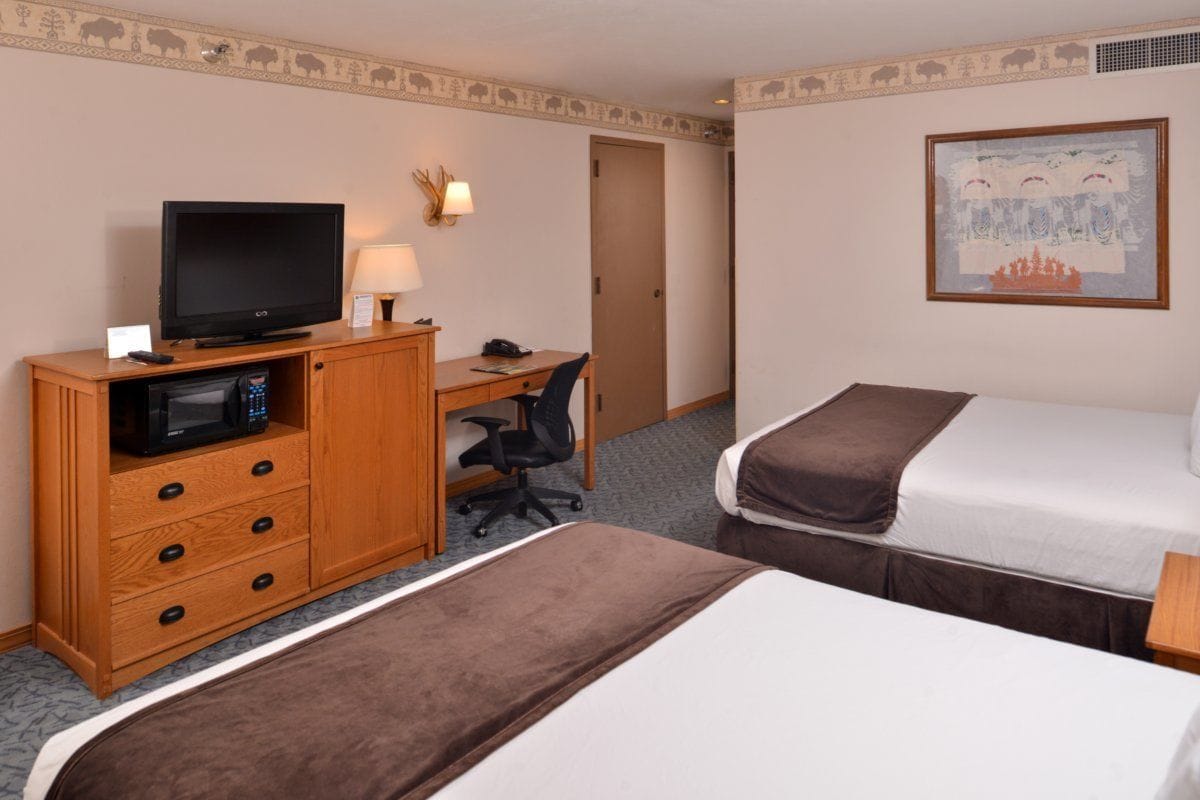 Ein Hotelzimmer mit zwei Betten, einem Schreibtisch mit Computer, Fernseher und einer Mikrowelle.