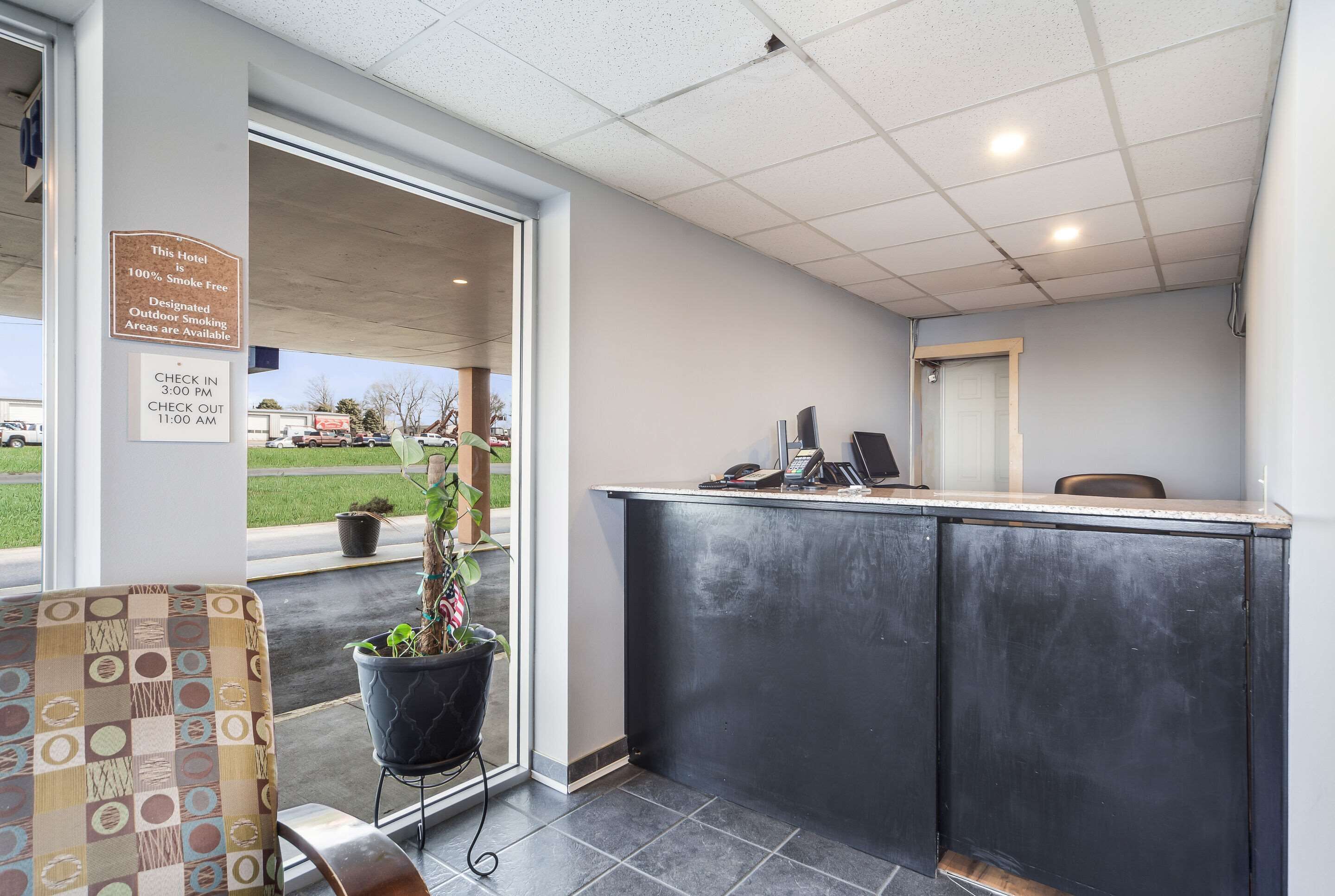 A hotel reception area with a check-in/check-out desk, a potted plant, and a view of the outside.