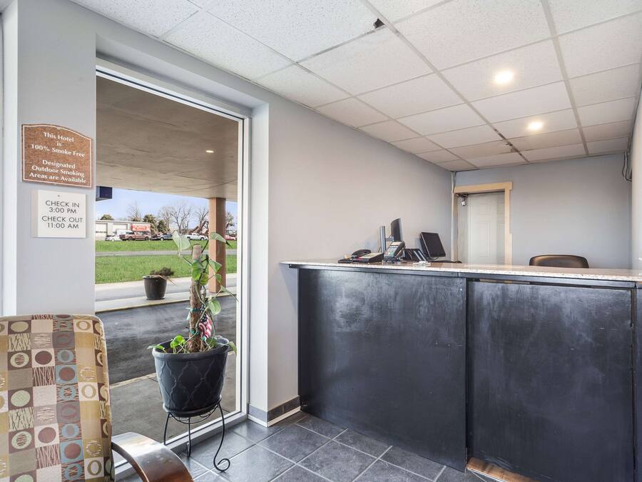 A hotel reception area with a check-in/check-out desk, a potted plant, and a view of the outside.