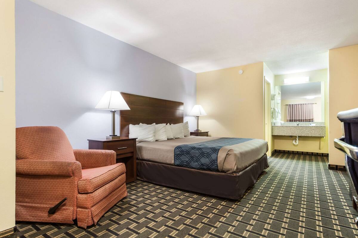 A hotel room with a bed, a chair, a nightstand, and a lamp.