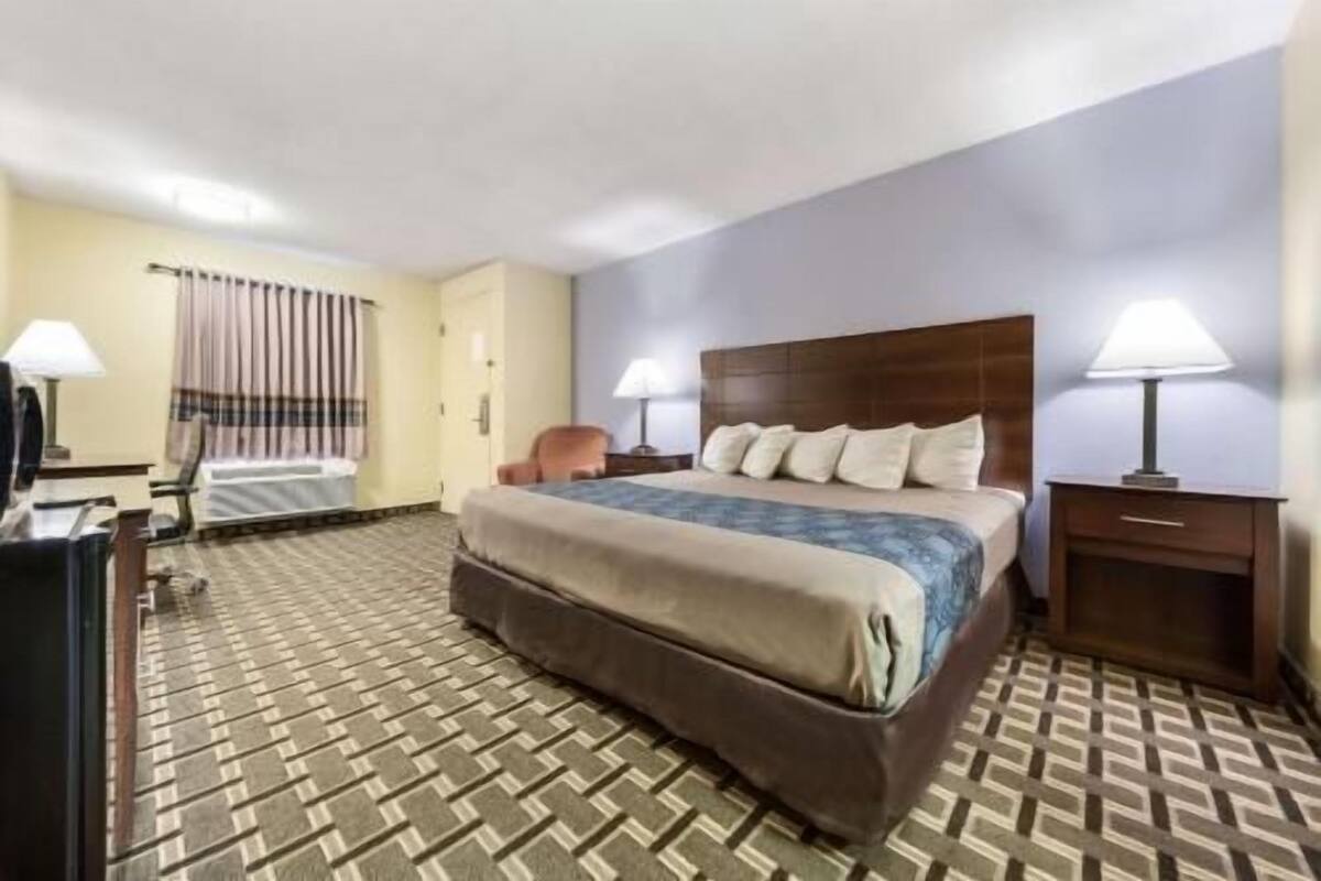 A hotel room with a large bed, a chair, a desk, and a lamp.