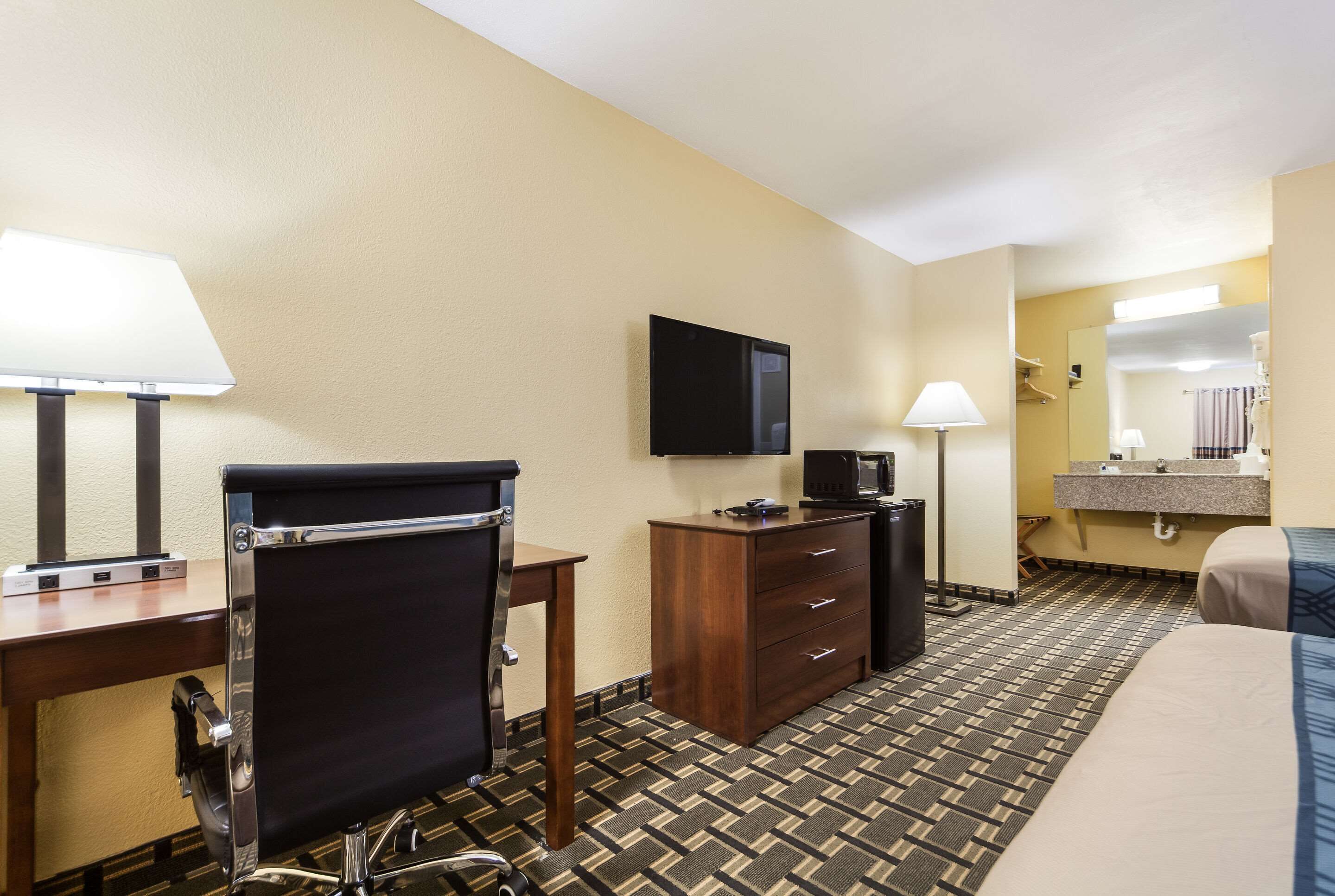 A hotel room with a bed, desk, chair, TV, and a small kitchenette.