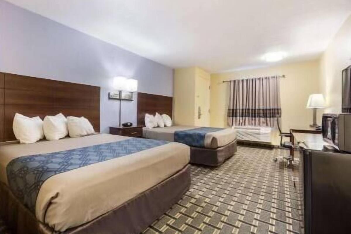 A hotel room with two beds, a desk, a television, and a window with curtains.