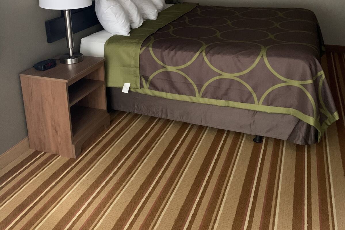 Une chambre d’hôtel avec un lit, deux lampes de chevet, une table de nuit, un tableau encadré au mur et un tapis à rayures.