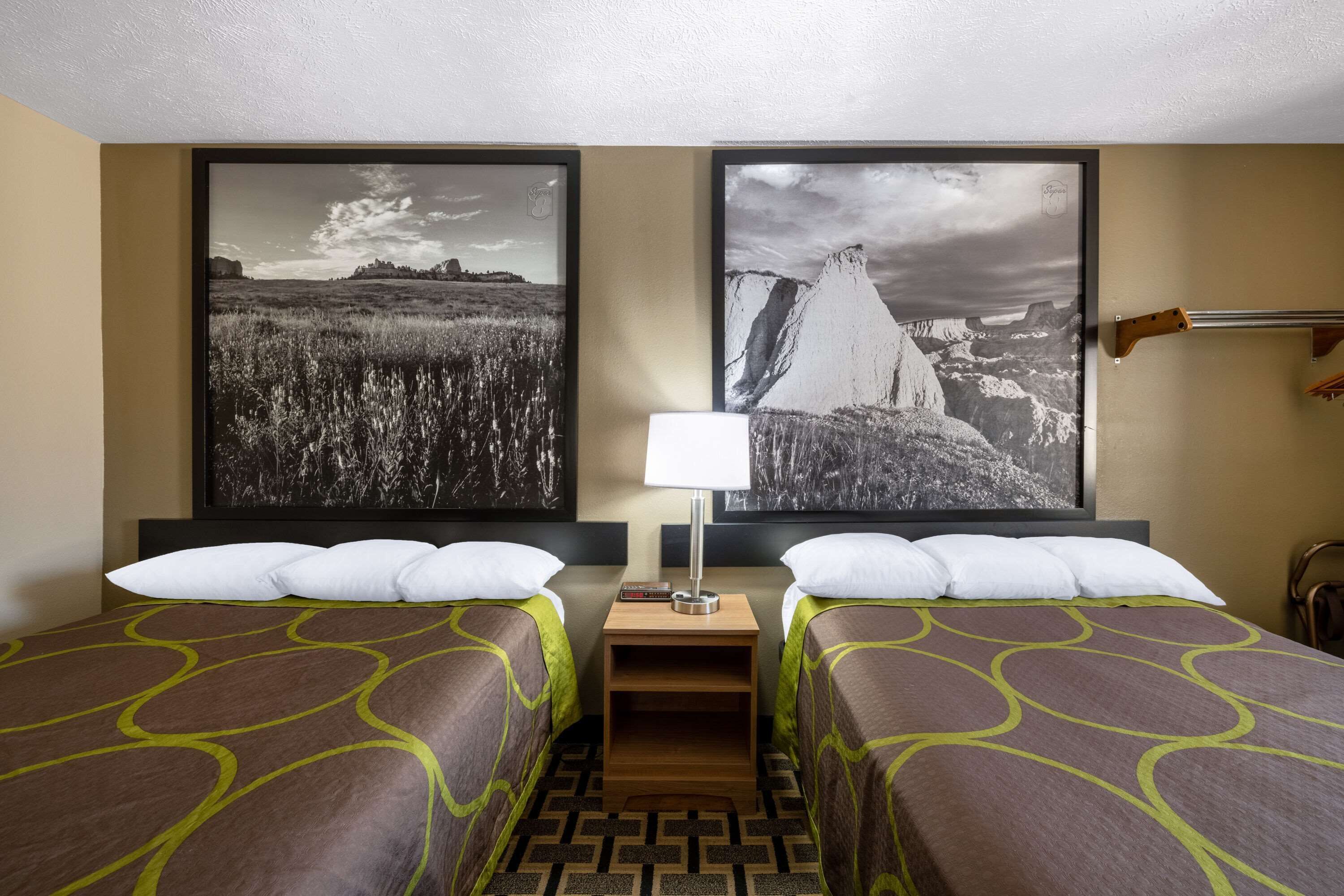 Camera d'albergo con due letti, un comodino con una lampada e due grandi fotografie di paesaggi appese al muro.