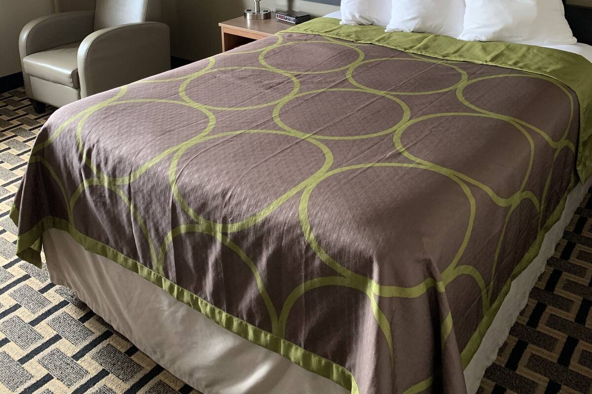 Une chambre d’hôtel avec un grand lit, une chaise, une table de chevet, une lampe et un téléviseur fixé au mur.