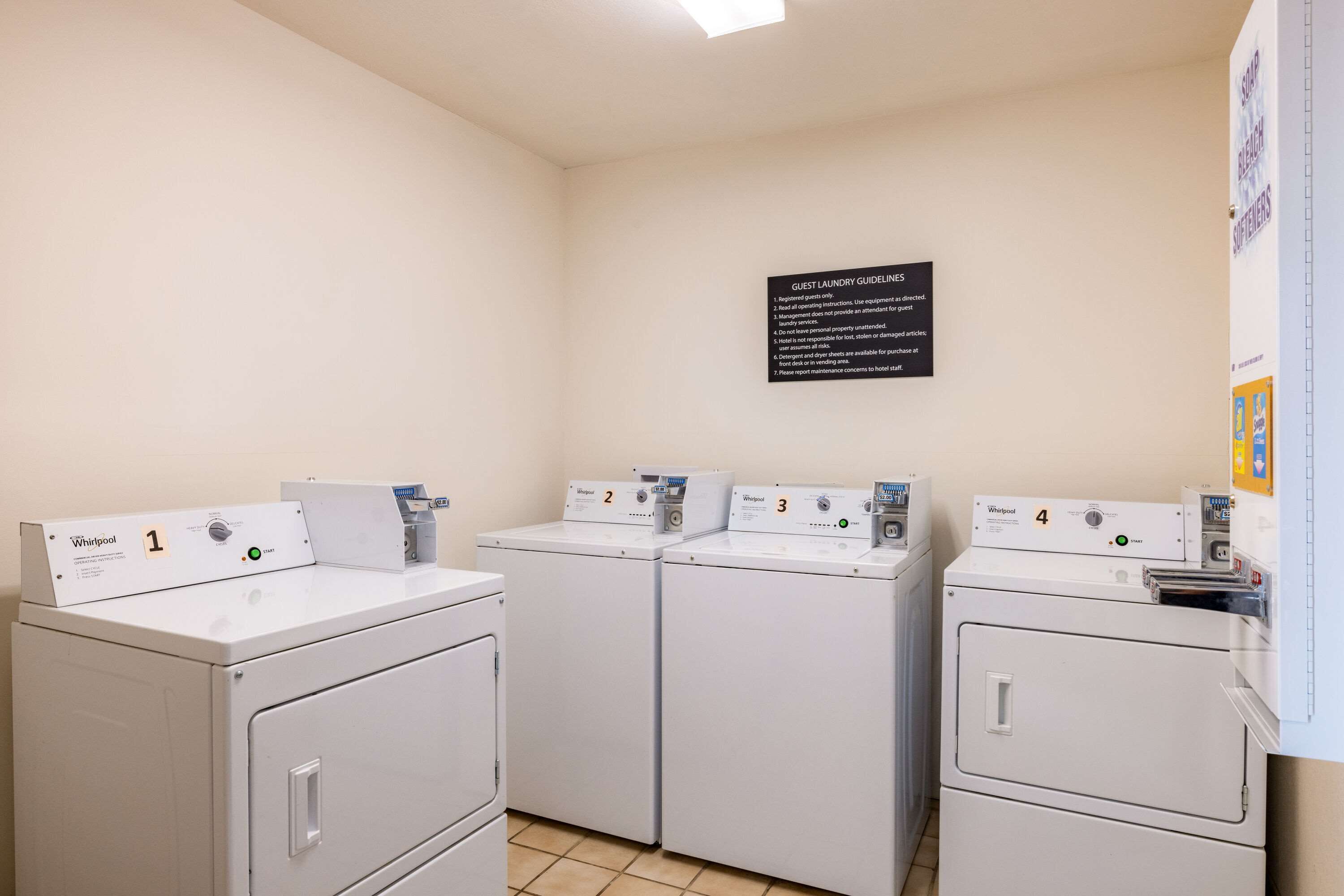 A laundry area with four Whirlpool washers, numbered 1 to 4, and a sign with guest laundry guidelines.