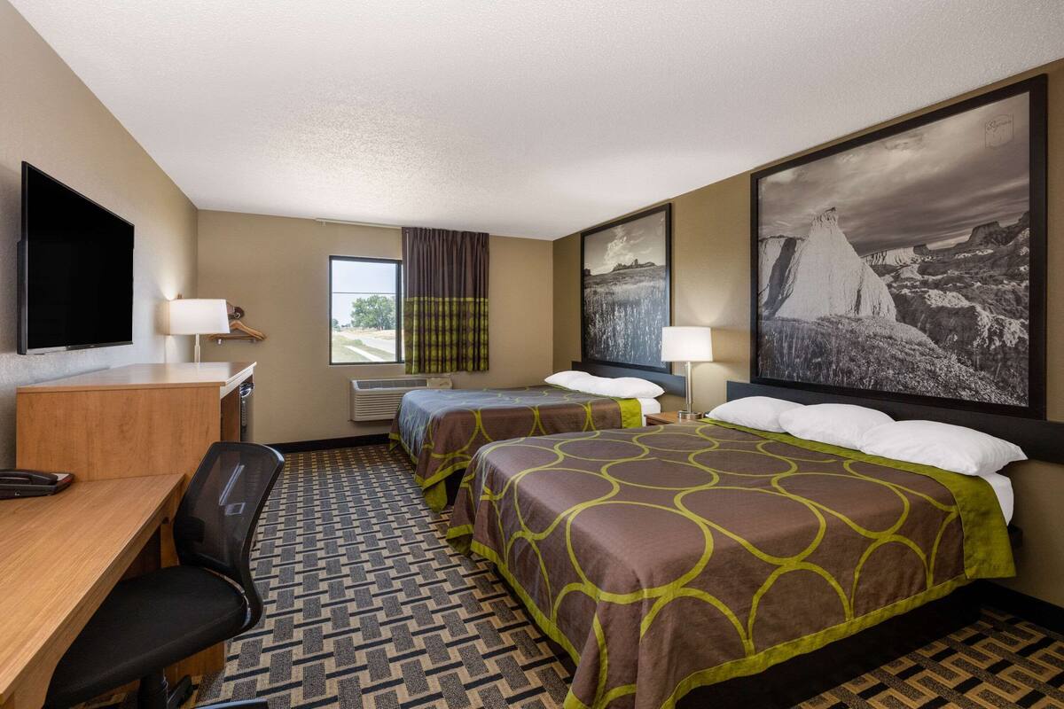 Une chambre d’hôtel avec deux lits, un bureau, une chaise, une télévision et un grand tableau au mur.