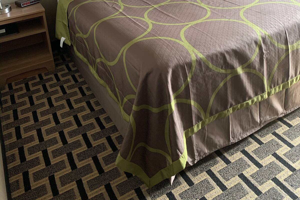 Une chambre d’hôtel avec un grand lit, une table de chevet avec une lampe, un téléviseur fixé au mur et un grand tableau encadré représentant un paysage de montagne.
