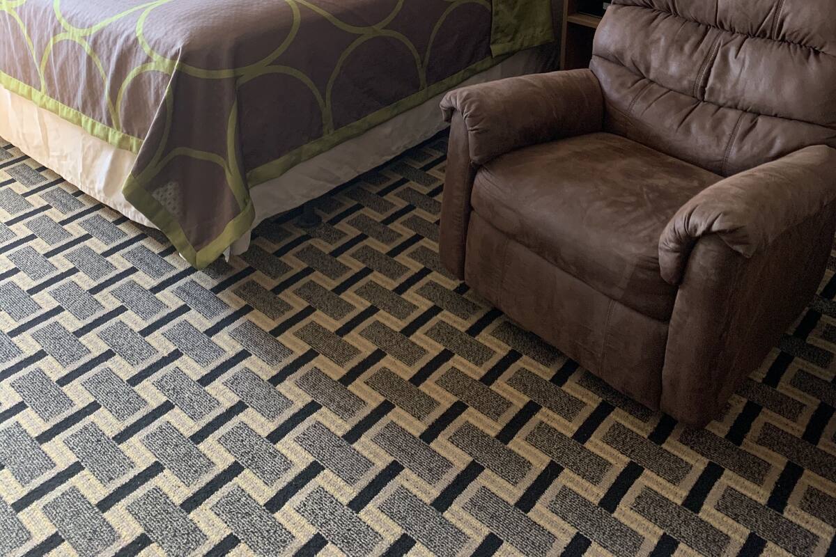 Une chambre d’hôtel avec un lit, deux lampes de chevet, un fauteuil en cuir marron, une moquette à motifs et un grand tableau représentant un paysage accroché au mur.