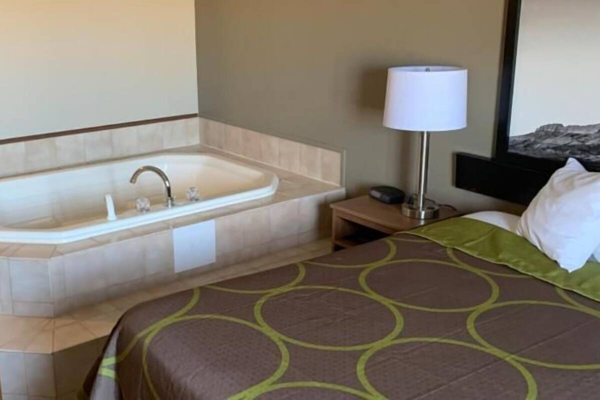 Une chambre d’hôtel avec une baignoire, une lampe de chevet, un lit avec une couvre-lit à motifs et une table de chevet.