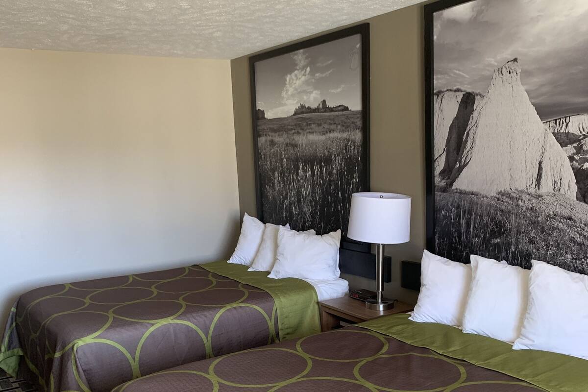 Une chambre d’hôtel avec deux lits, une table de chevet avec une lampe et deux grandes peintures représentant des paysages accrochées au mur.