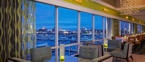 A modern dining area with large windows, a view of the marina, and a unique chandelier.