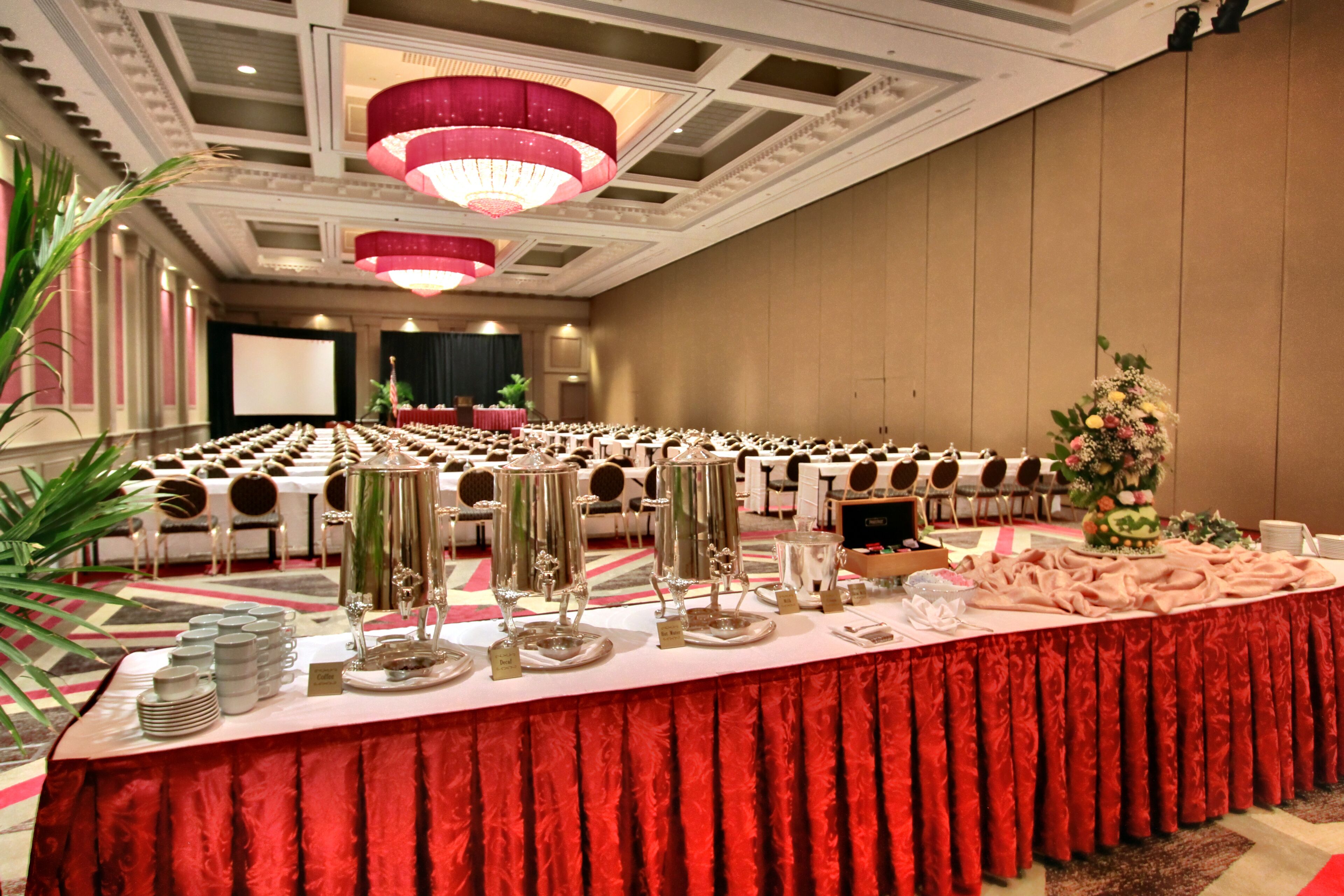A banquet hall with rows of tables, a stage, and a large floral arrangement.