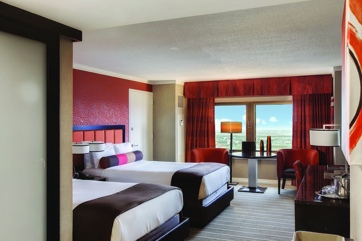 A hotel room with two beds, a desk, a chair, and a window with a view.