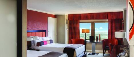A hotel room with two beds, a desk, a chair, and a window with a view.