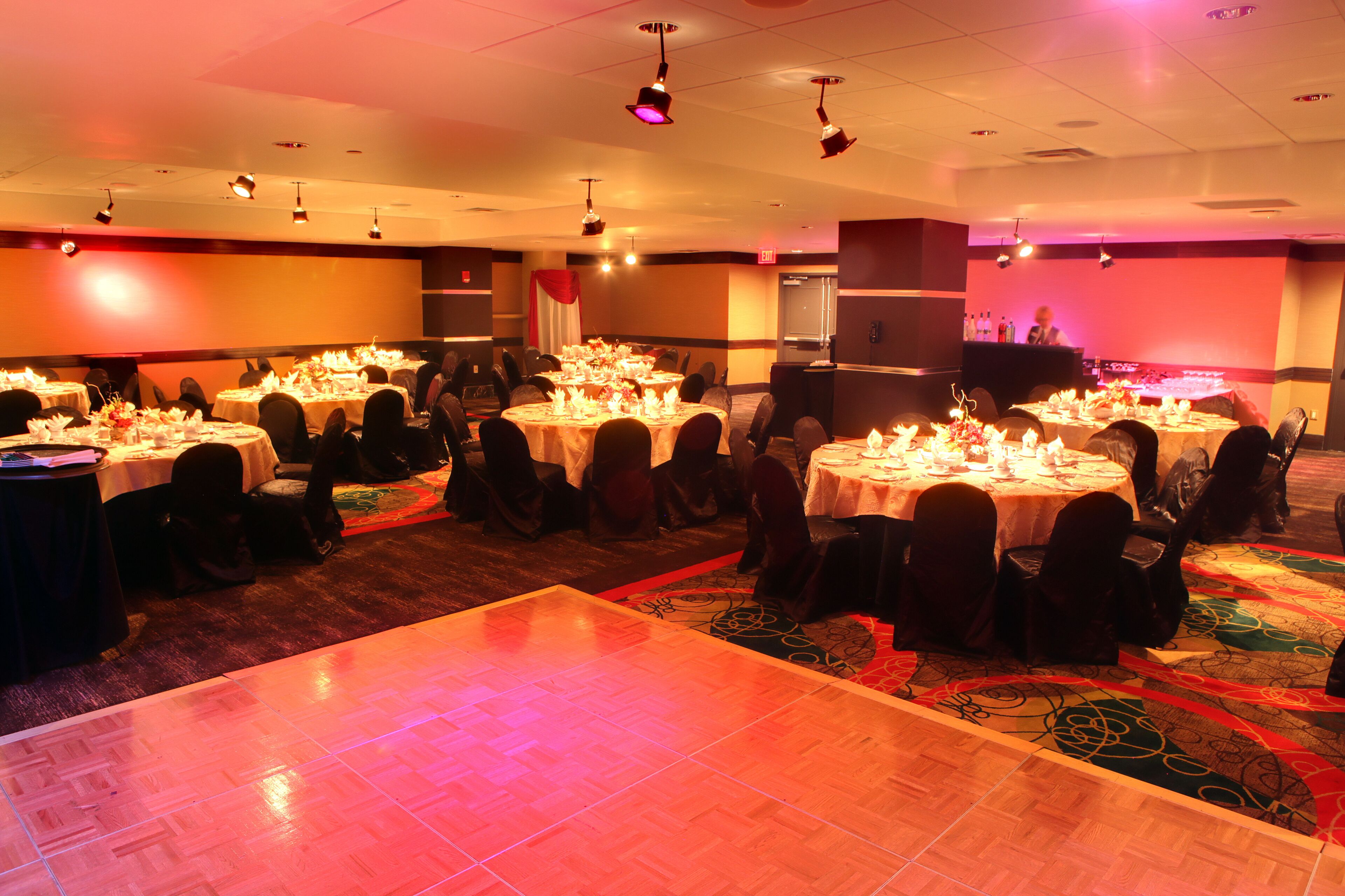 Un salón de banquetes con mesas redondas dispuestas para cenar, una pista de baile y una zona de bar.