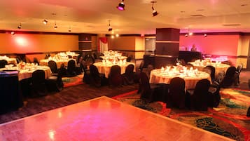 Un salón de banquetes con mesas redondas dispuestas para cenar, una pista de baile y una zona de bar.
