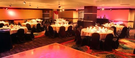 Una sala da banchetti con tavoli rotondi apparecchiati per la cena, una pista da ballo e un'area bar.