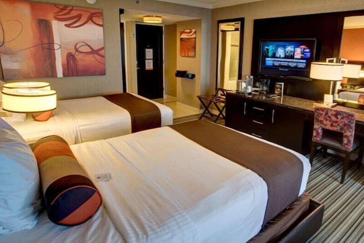 A hotel room with two beds, a desk, a television, and a mirror.