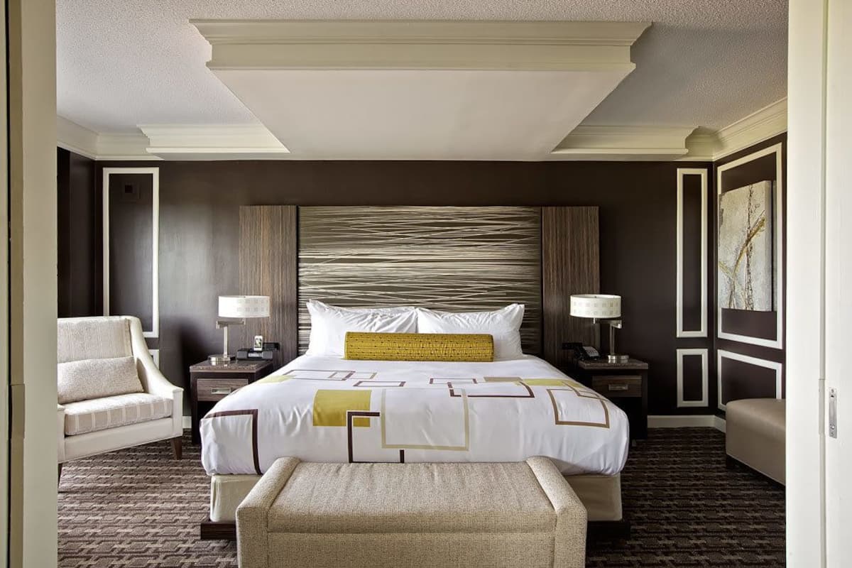 A hotel room with a large bed, two bedside tables with lamps, a chair, and a bench.