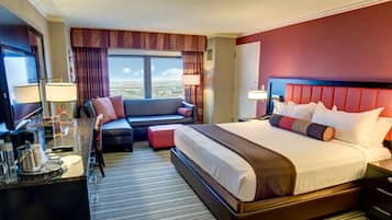A hotel room with a large bed, a sofa, a TV, and a desk with a lamp.