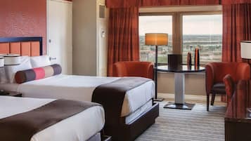 A hotel room with two beds, a desk with a lamp, a chair, and a view of the city.