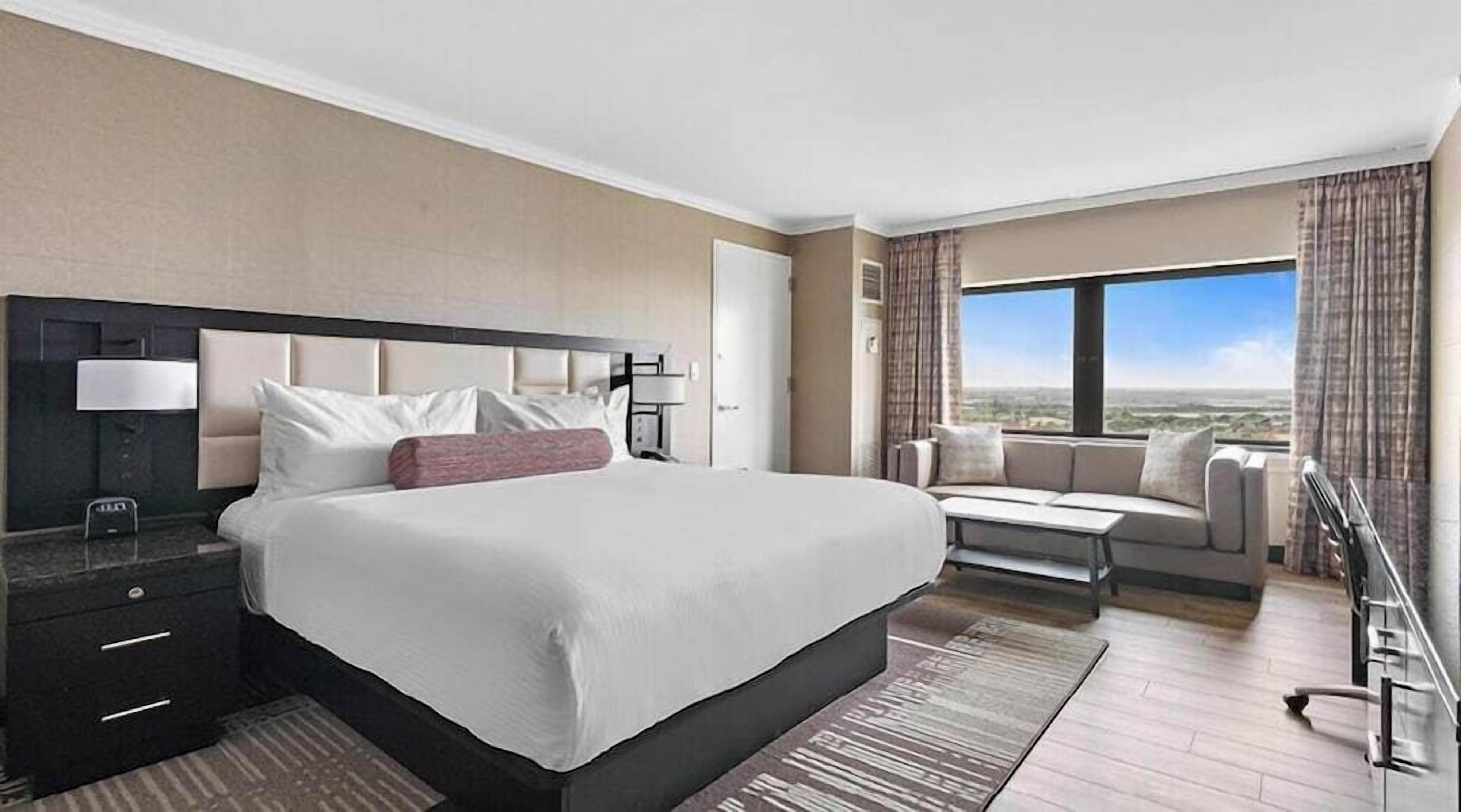 Une chambre d’hôtel avec un grand lit, un bureau avec une lampe, un canapé et une vue sur le paysage.