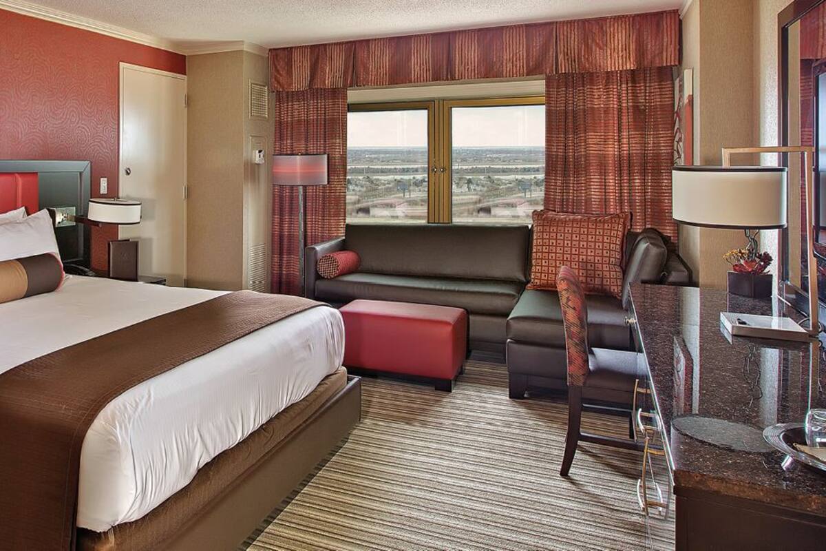A hotel room with a large bed, a sofa, a desk, and a view of the city.