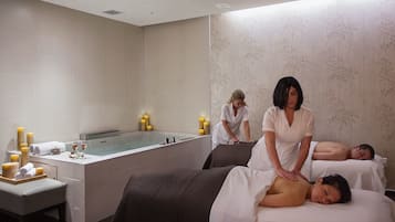 A spa room with a massage table, a bathtub, and candles.