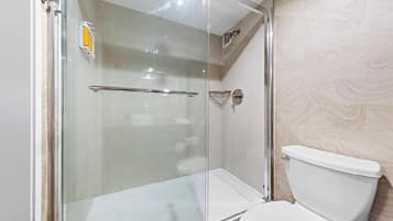 A modern bathroom with a glass-enclosed shower, a white toilet, and a marble-patterned wall.