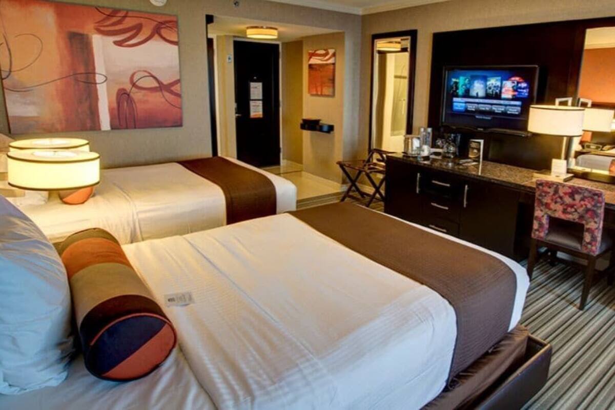 A hotel room with two beds, a desk with a television, a mirror, and a carpeted floor.