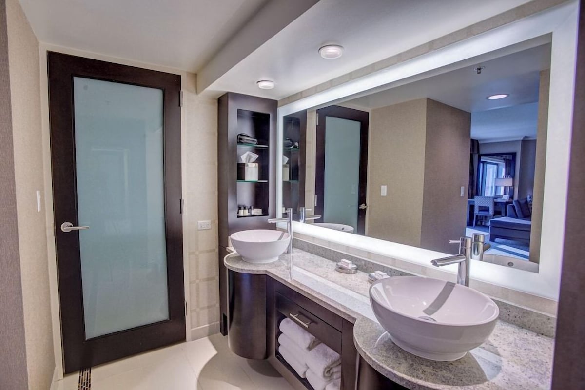 A modern bathroom with two vessel sinks, a large mirror, and a dark door.