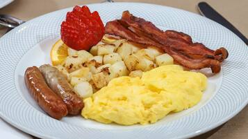 Ein Teller mit Rührei, Speck, Würstchen, Bratkartoffeln und einer Erdbeere.
