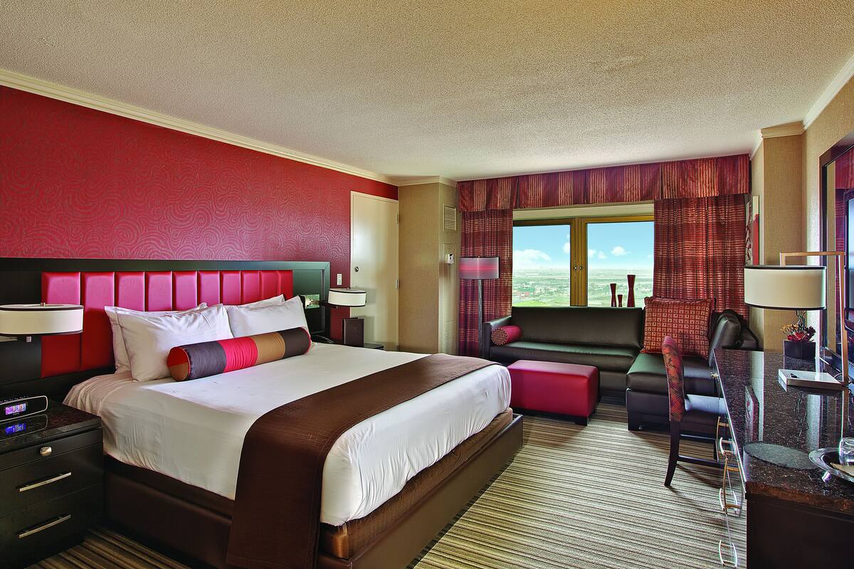 A hotel room with a large bed, a desk, a chair, and a view of the cityscape.