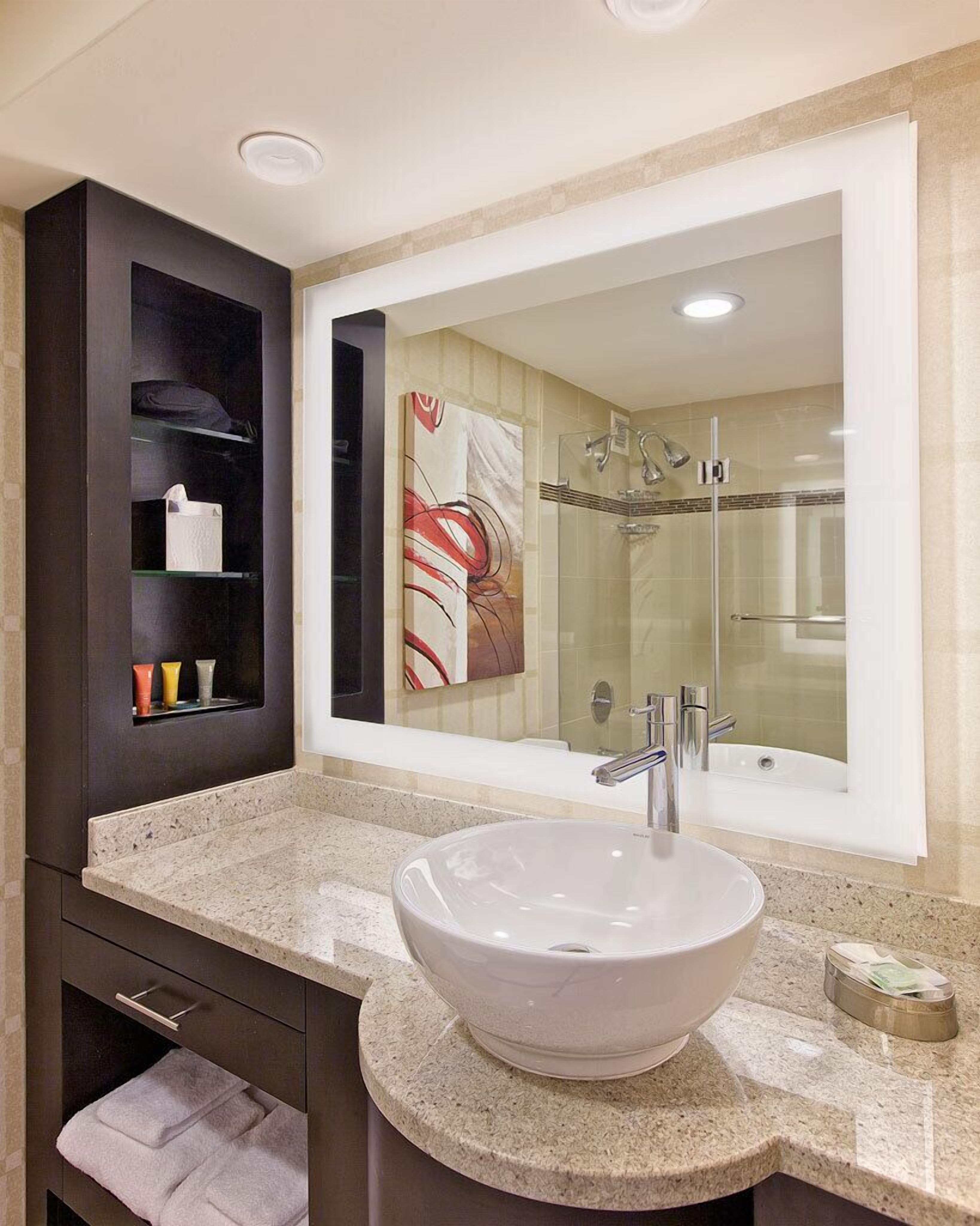 Un baño moderno con un espejo grande, un lavamanos tipo recipiente y una ducha con mampara de vidrio.