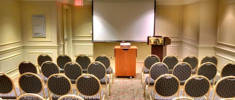 A conference room with rows of patterned chairs, a podium, and a projection screen.