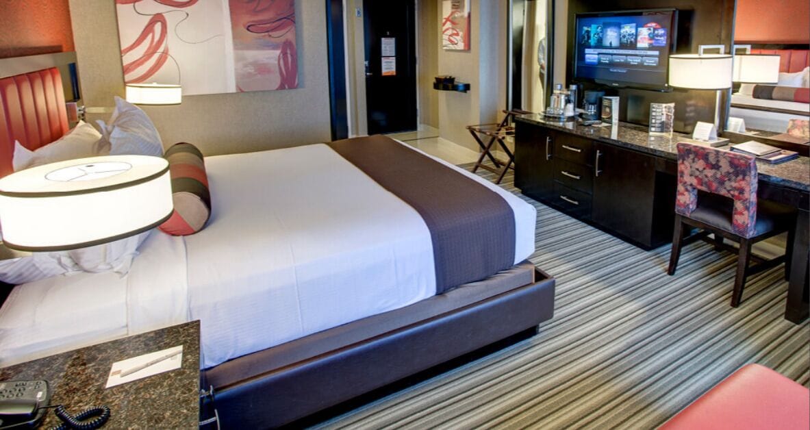 A hotel room with a large bed, a desk with a chair, a television, and a minibar.