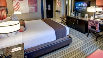 A hotel room with a large bed, a desk with a chair, a television, and a minibar.