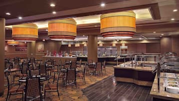 Un espace buffet comprenant plusieurs stands de nourriture, des tables rondes et des chaises.